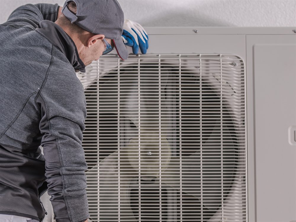 Technicien nettoyant la grille d'une unité extérieure de thermopompe